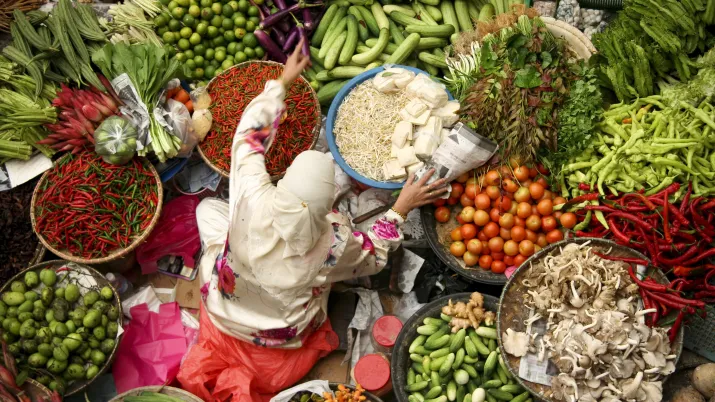 Vendeuse assise entourée de ses paniers de fruits et légumes.