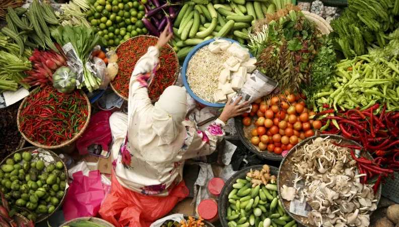 Vendeuse assise entourée de ses paniers de fruits et légumes.